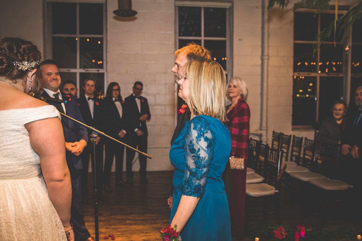 Wedding guests mingling and dancing at an indoor reception venue with string lights.