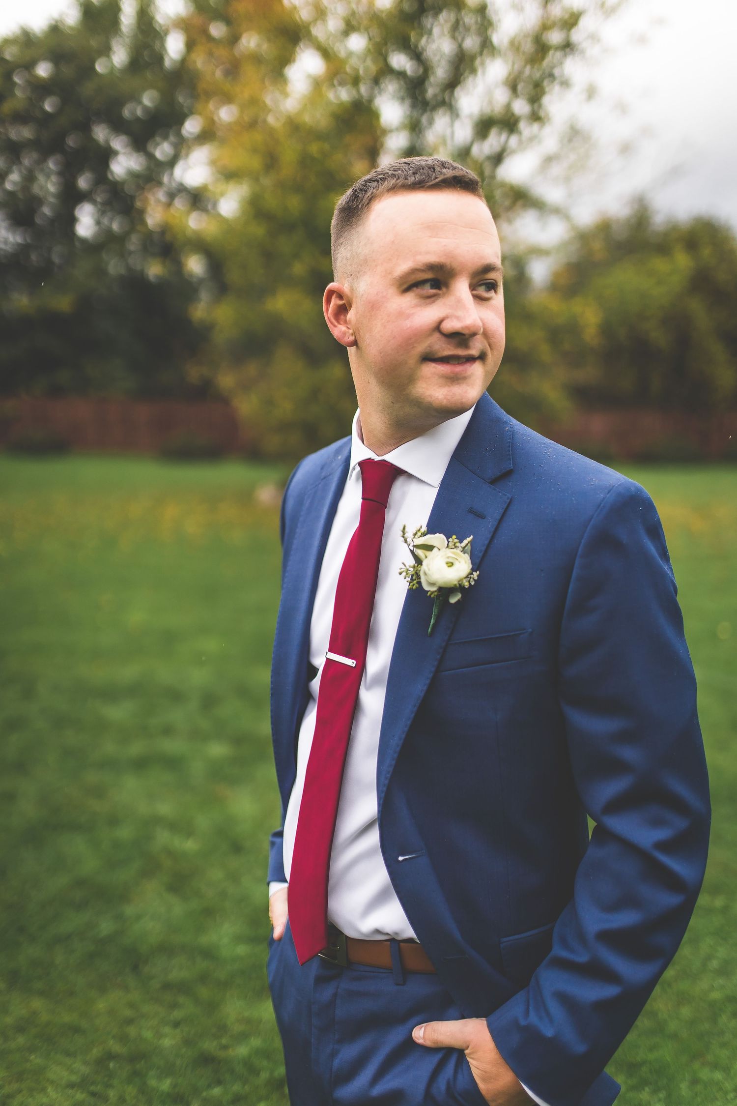 Groomsman in navy suit and burgundy tie poses in outdoor fall setting.