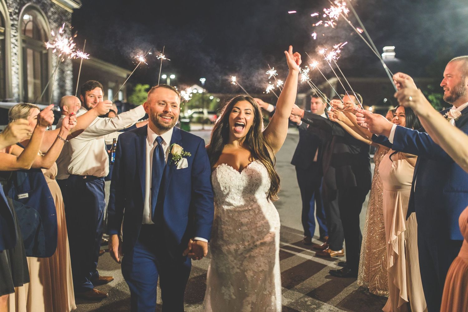 Wedding guests holding sparklers during nighttime celebration exit.