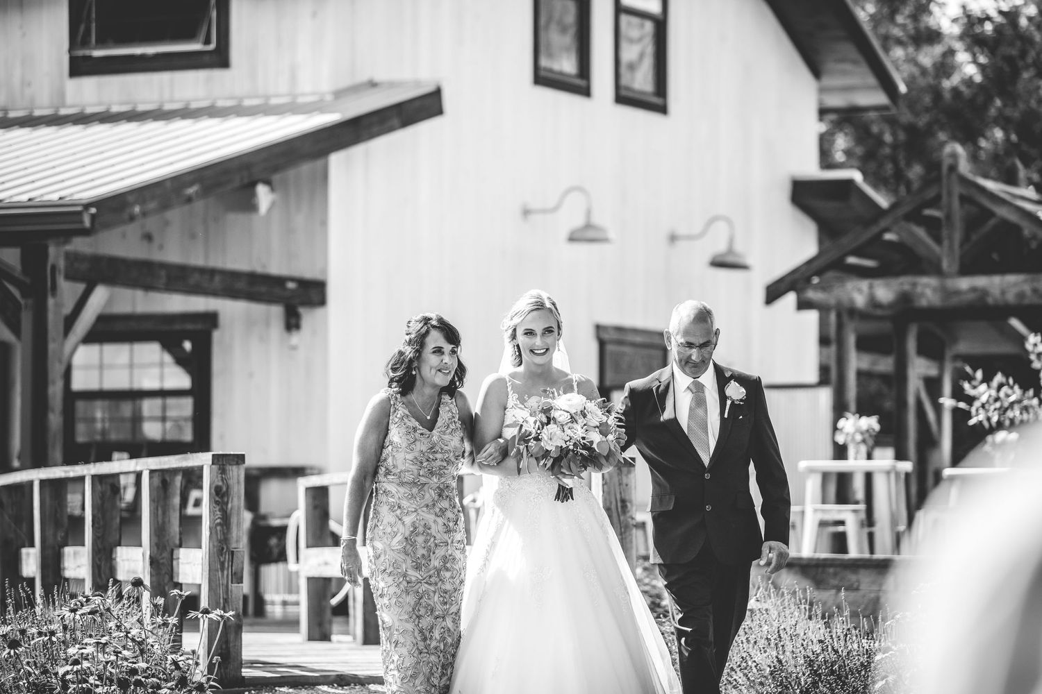 Black and white photo of a wedding processional outside a rustic farmhouse venue.