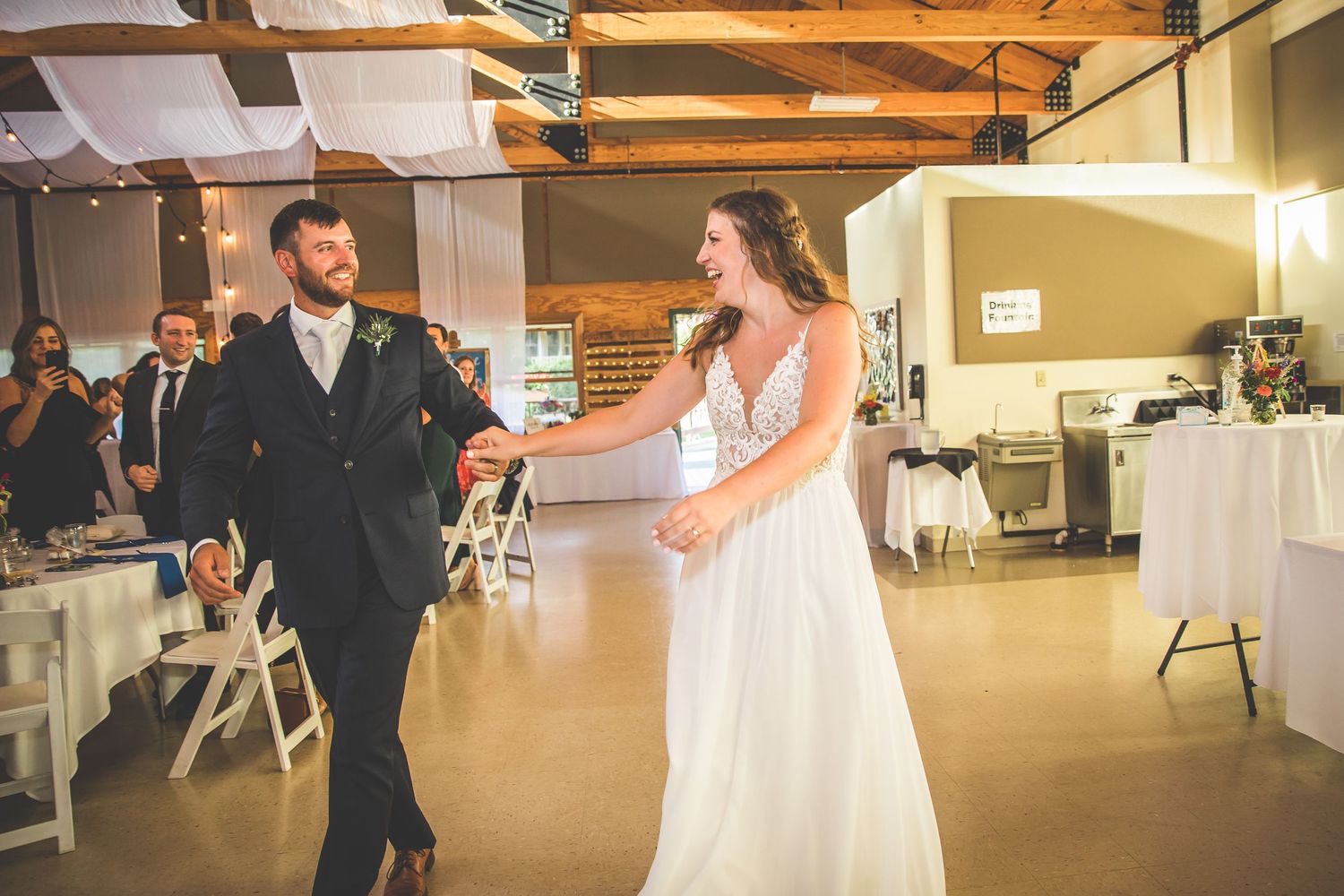 Wedding couple shares their first dance in a rustic venue decorated with white draping and hanging lanterns.