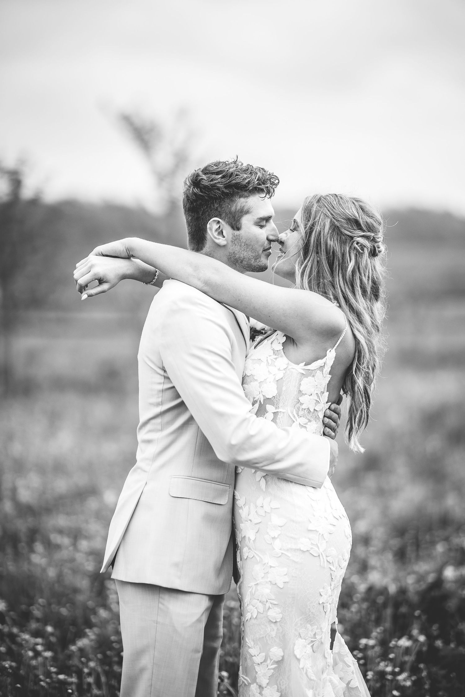 Black and white portrait of newlyweds sharing intimate moments in a rustic field.