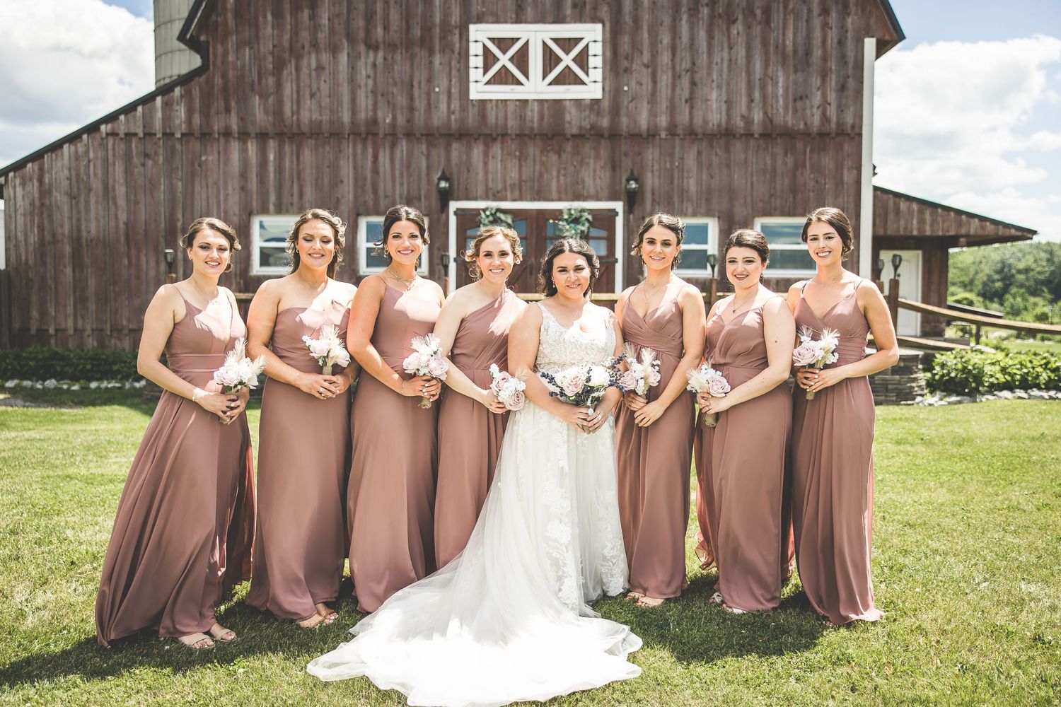 Wedding party lined up in front of a rustic brown barn with white trim.