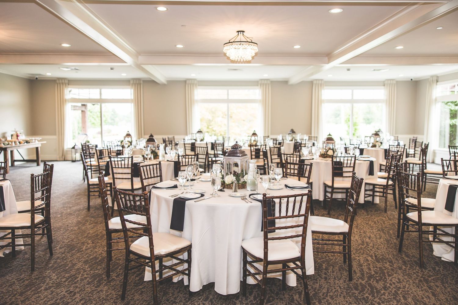 Spacious wedding reception venue with white tablecloths and dark wooden chairs arranged in banquet style.