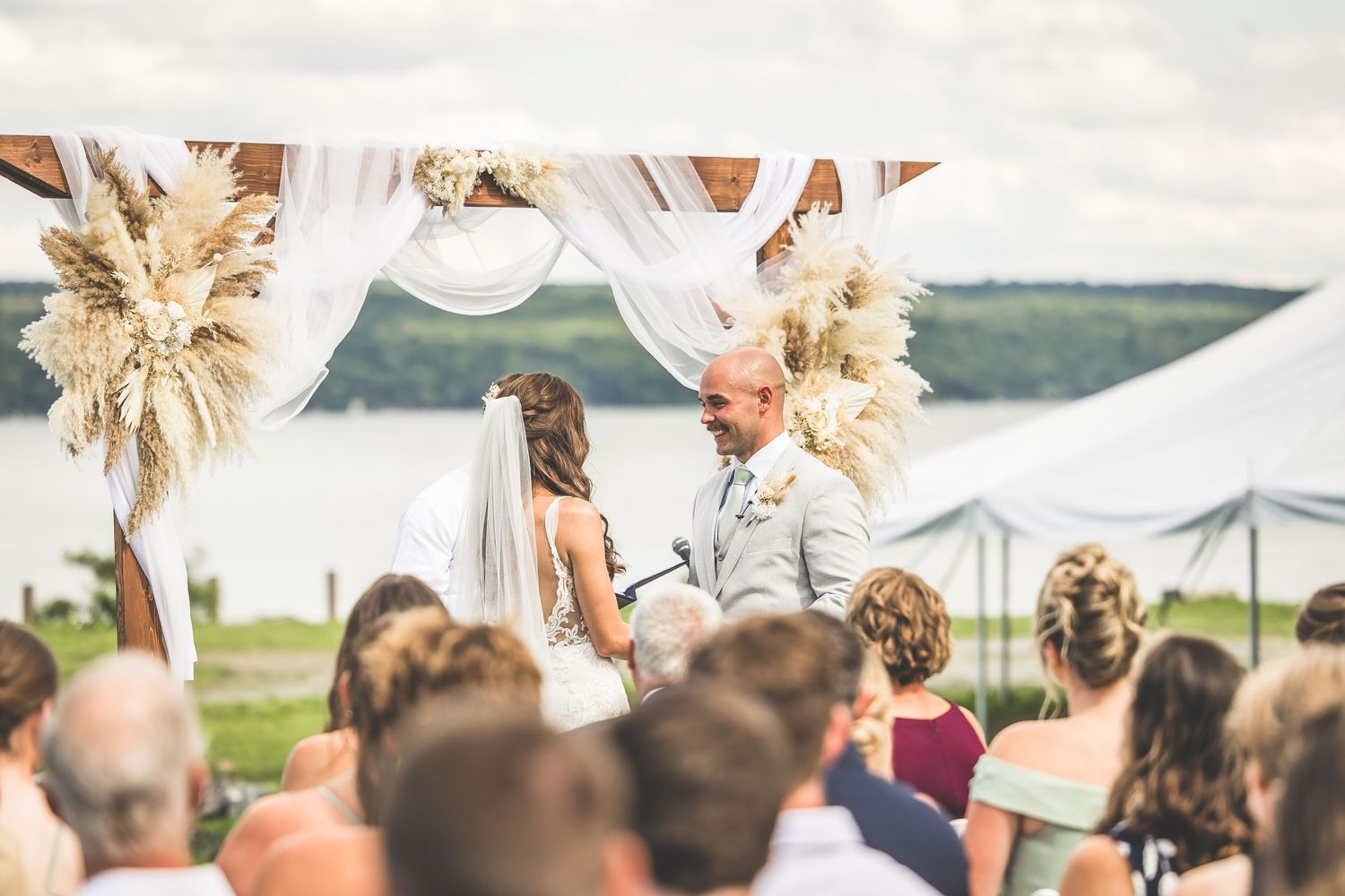 Wedding guests seated outdoors watching ceremony with water and mountains in background.