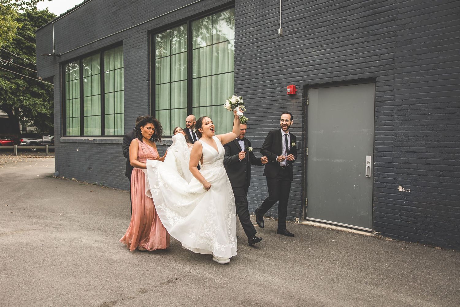 Wedding party members in formal attire gather outside a modern building.