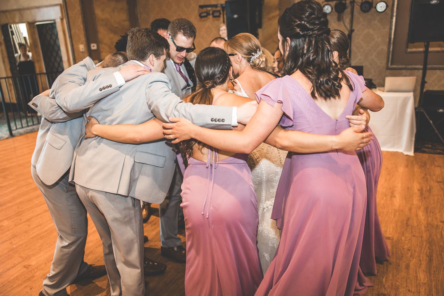 Wedding party forms a group hug on the dance floor in coordinated gray and purple attire.