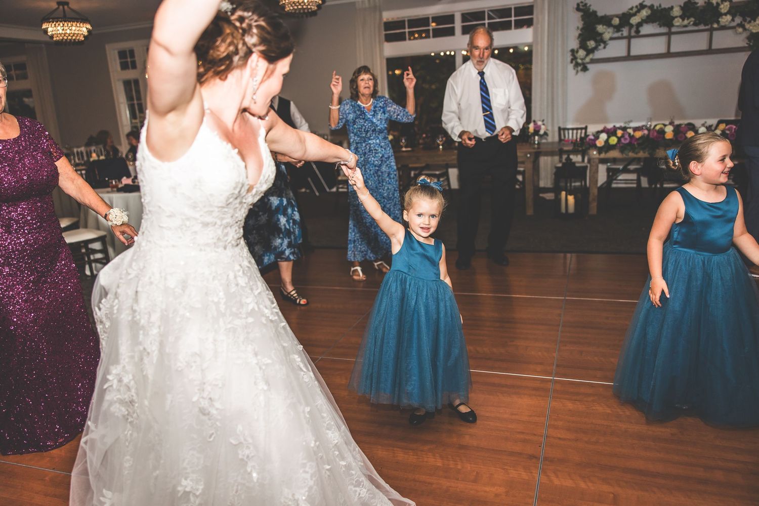 Wedding reception with bridesmaids in blue dresses dancing on wooden floor.