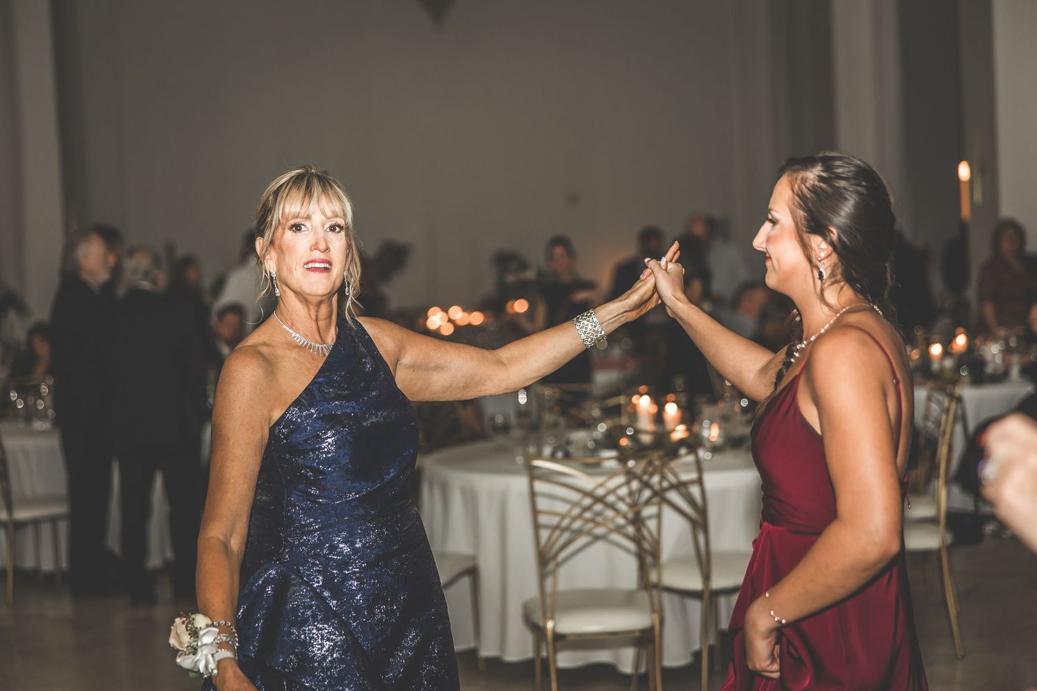 Wedding party members in burgundy and navy dresses dance during an evening reception.