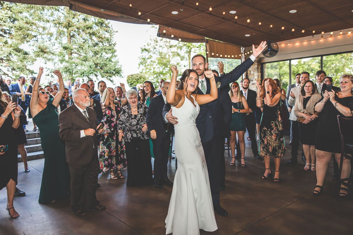 Wedding guests gathered on dance floor under string lights during reception celebration.