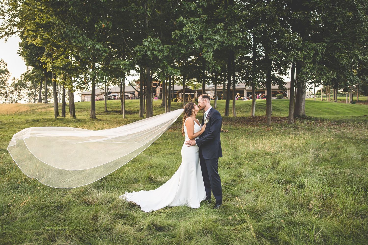 Flowing veil creates dramatic effect in outdoor wedding portraits on grassy path.