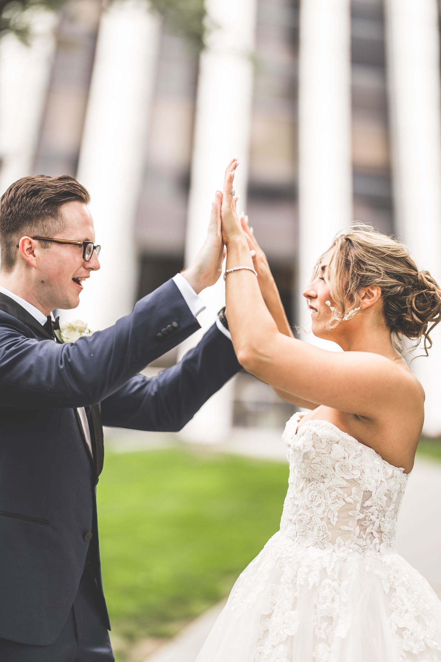 Newlyweds share a celebratory high-five moment in front of modern architecture.