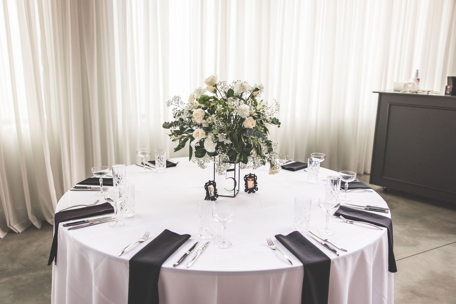 Round wedding reception table with white linens, place settings and floral centerpiece.