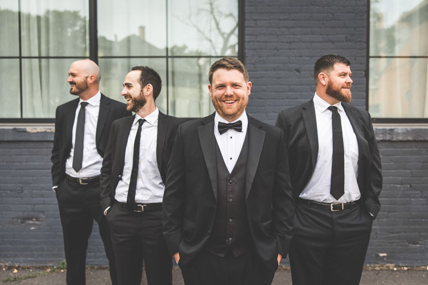 Wedding party members in formal attire stand together against a modern building exterior.
