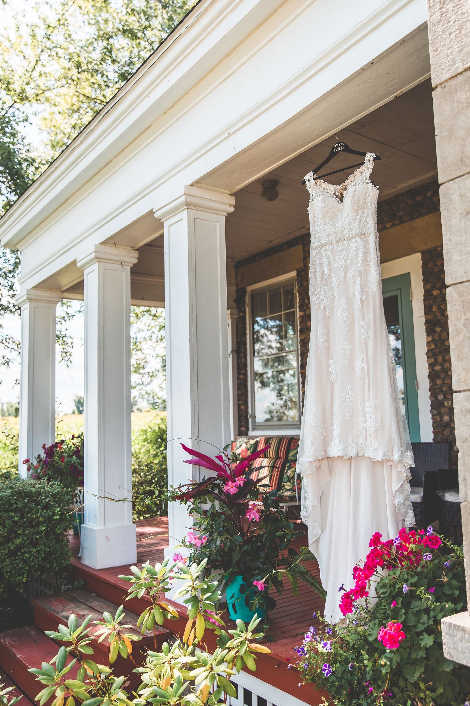 White wedding dress hanging on display with tropical flowers and columns in background.