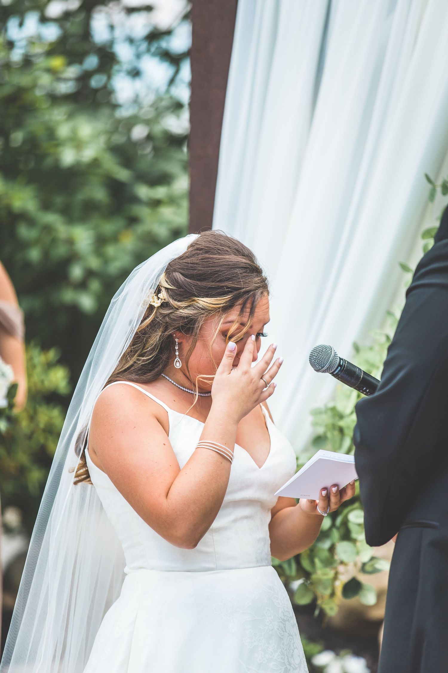 Emotional moment during outdoor wedding ceremony with white draping and microphone.