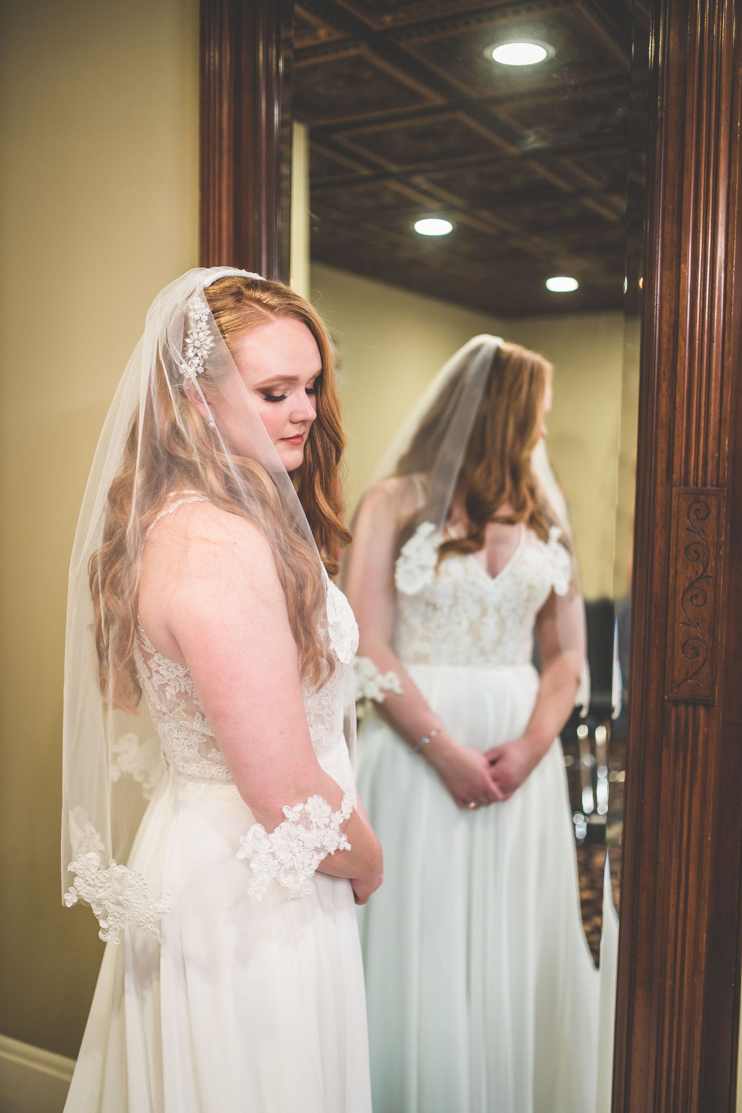 A bride admiring her wedding dress in an ornate mirror during final preparations.