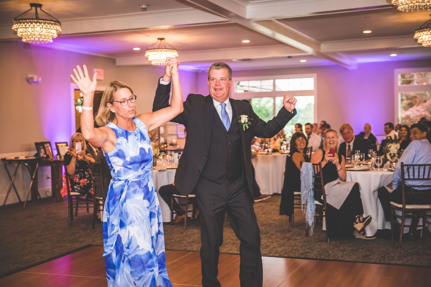 Wedding reception party with guests dancing and celebrating on the dance floor under crystal chandeliers.