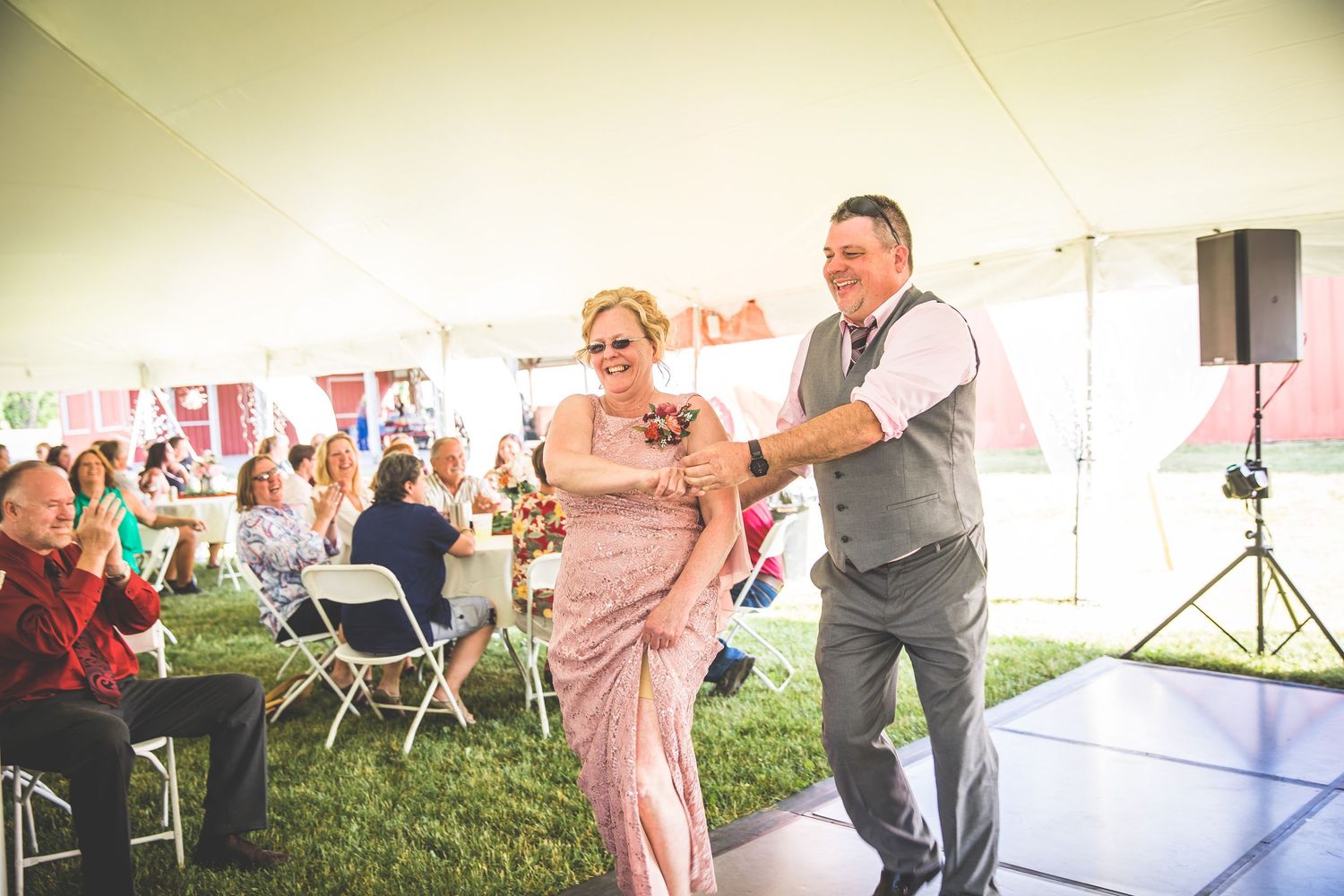 Guests dance together during a lively moment at an outdoor wedding reception under a white tent.