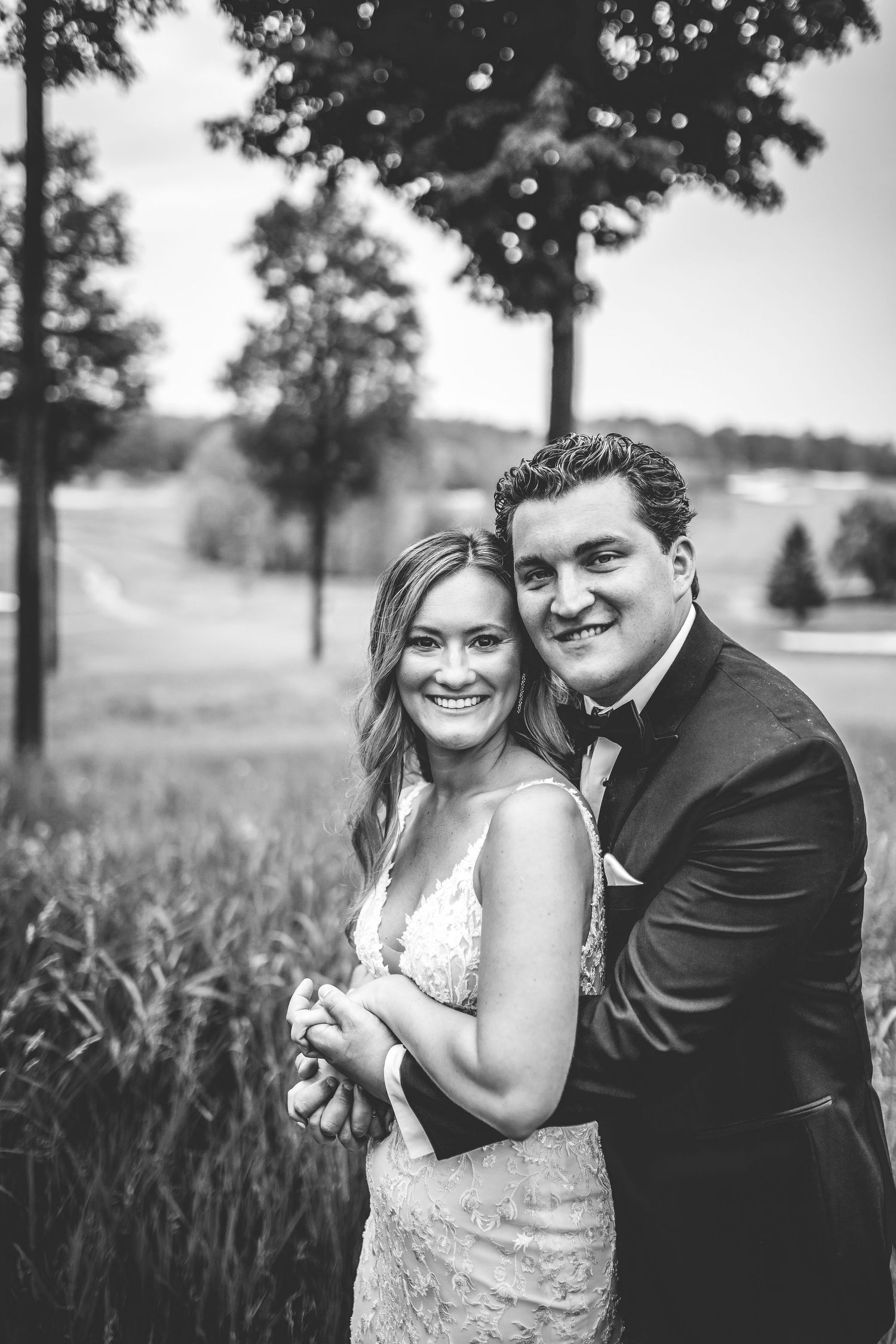 Black and white portrait of couple laughing together in outdoor field setting.
