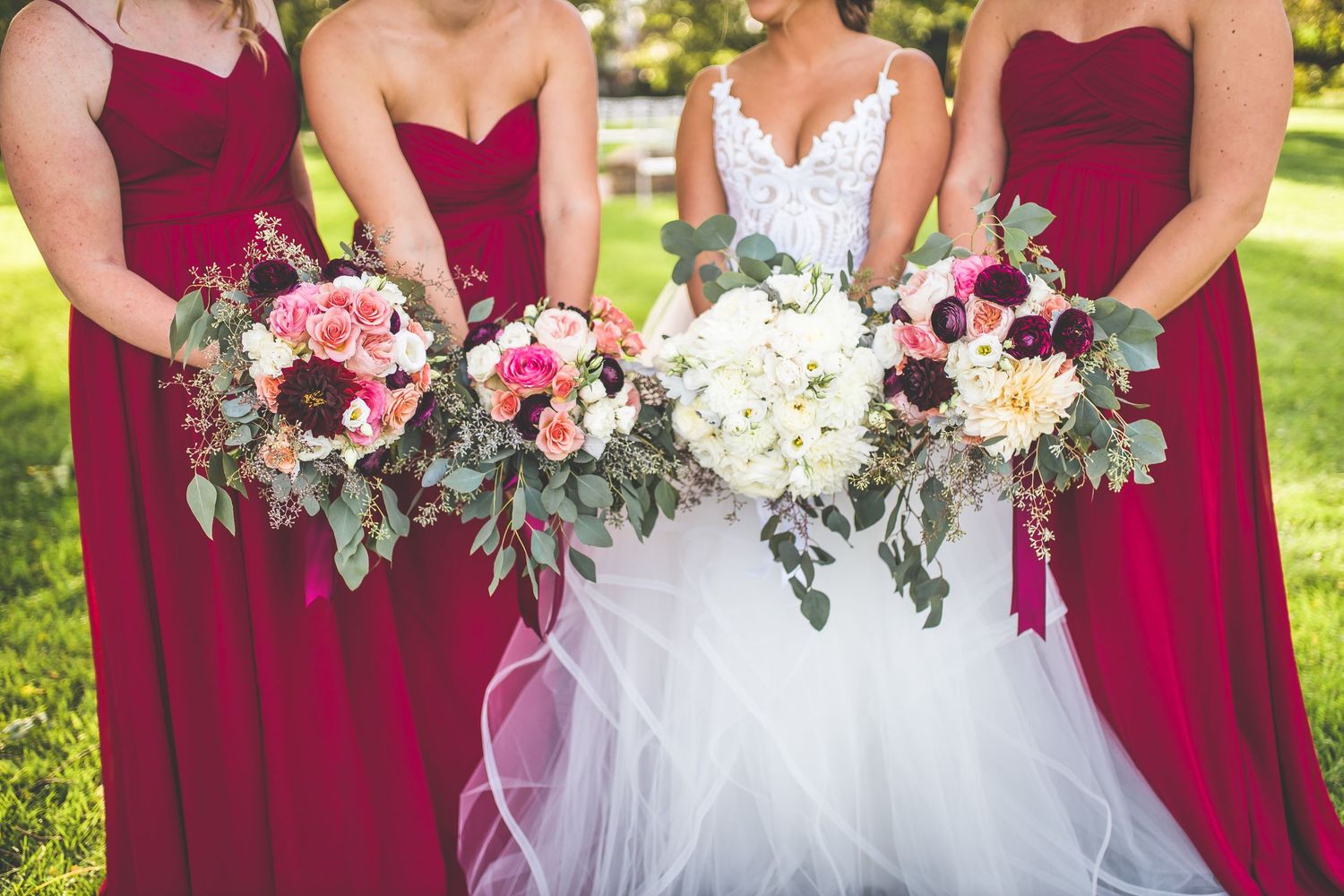 Bridal party holding elegant bouquets of pink and white flowers against burgundy bridesmaid dresses.