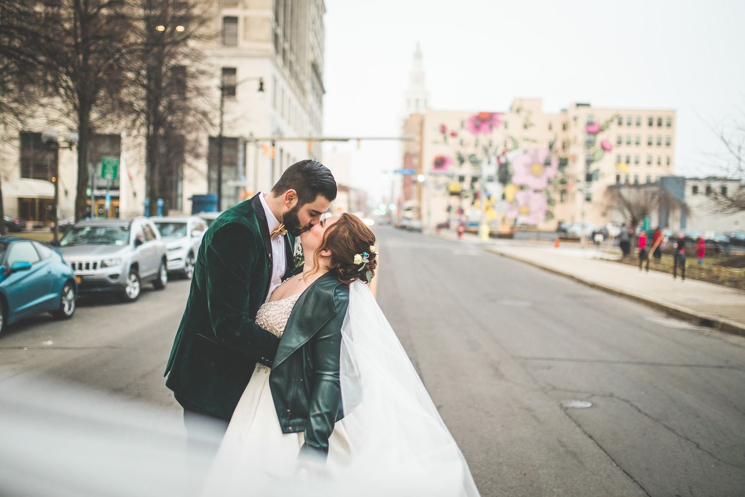 Romantic wedding couple sharing a kiss on an urban street with colorful buildings in the background.