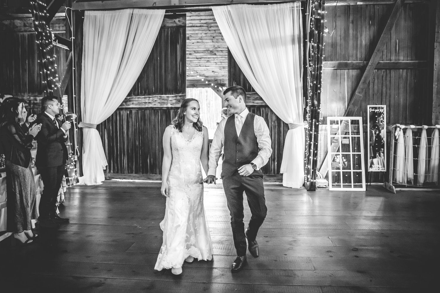 Black and white photo of elegant wedding ceremony setup with white drapes in rustic barn venue.