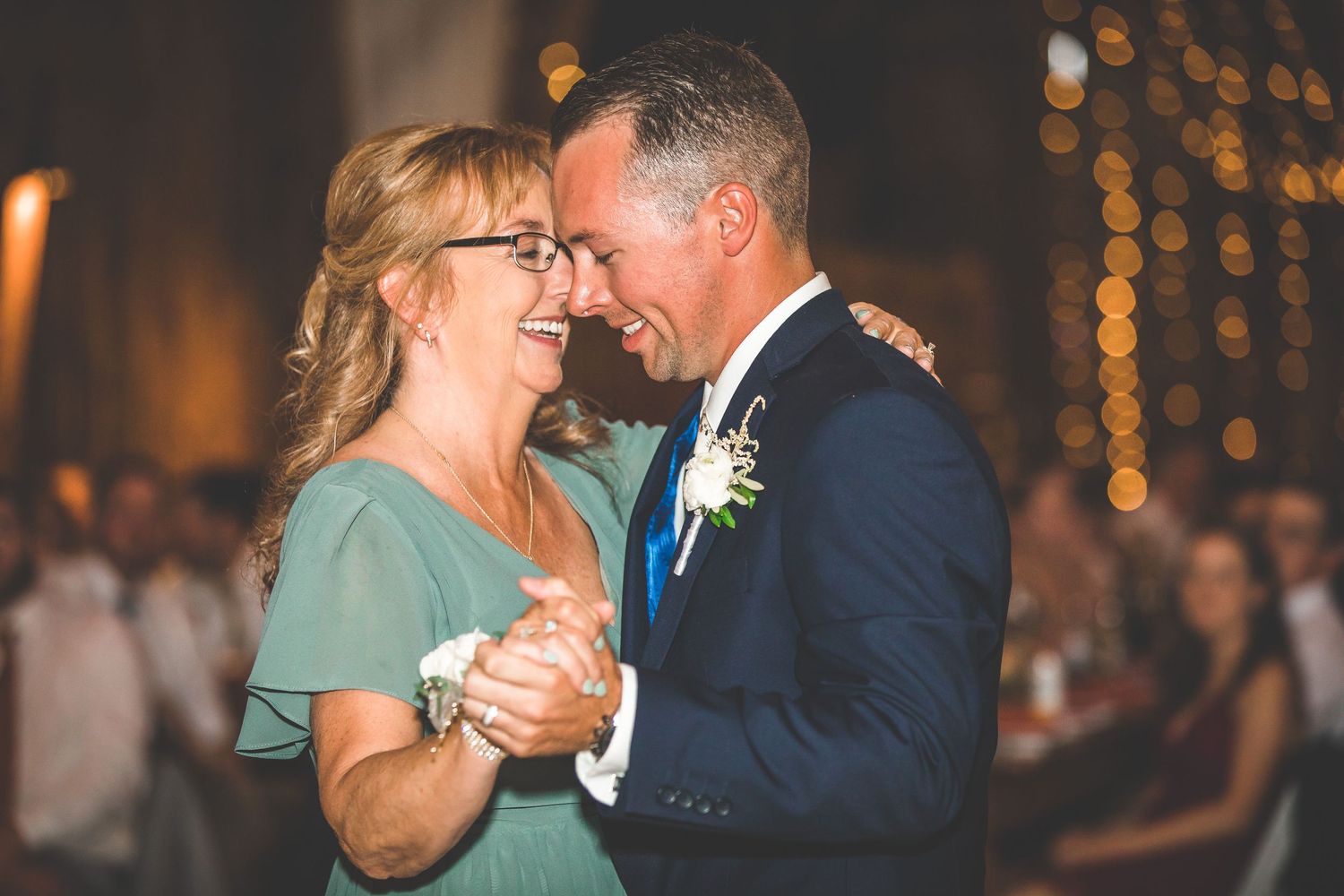 Couples dancing together during a wedding reception in a warmly lit barn venue.