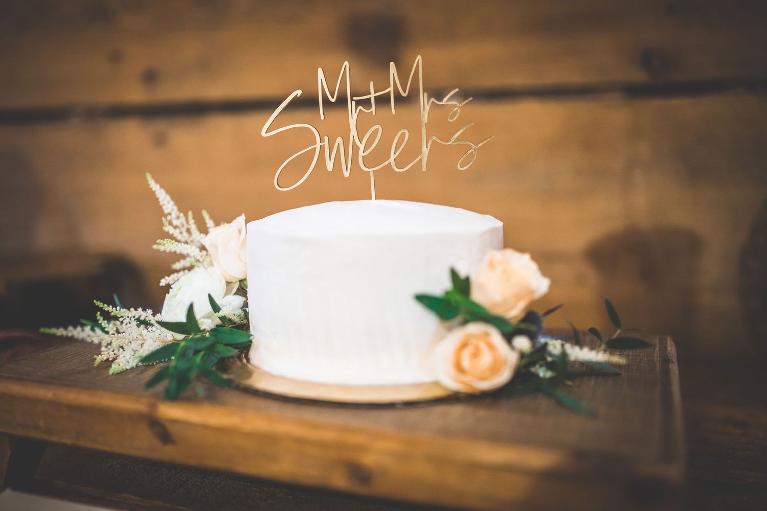 Wedding cake displayed on rustic wooden table with floral decorations.