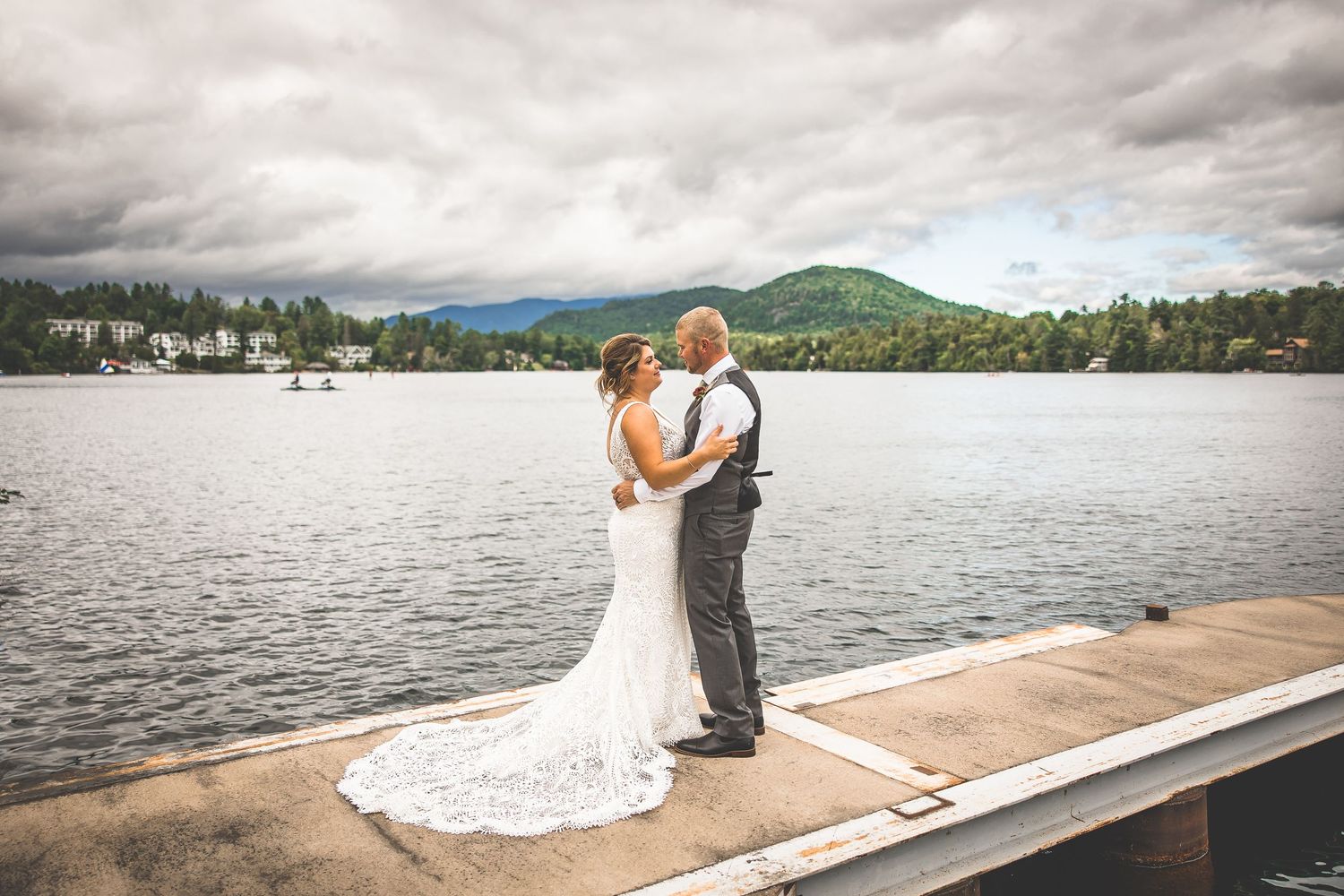 Newlyweds share romantic moments on a wooden dock overlooking a serene lake.