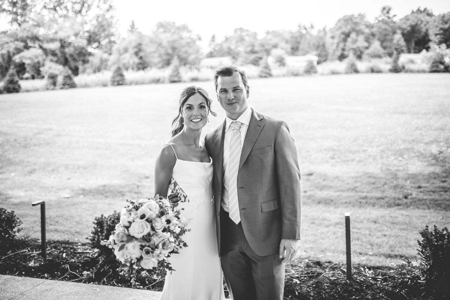 Newlyweds pose for portraits in sunlit garden with floral arrangements.