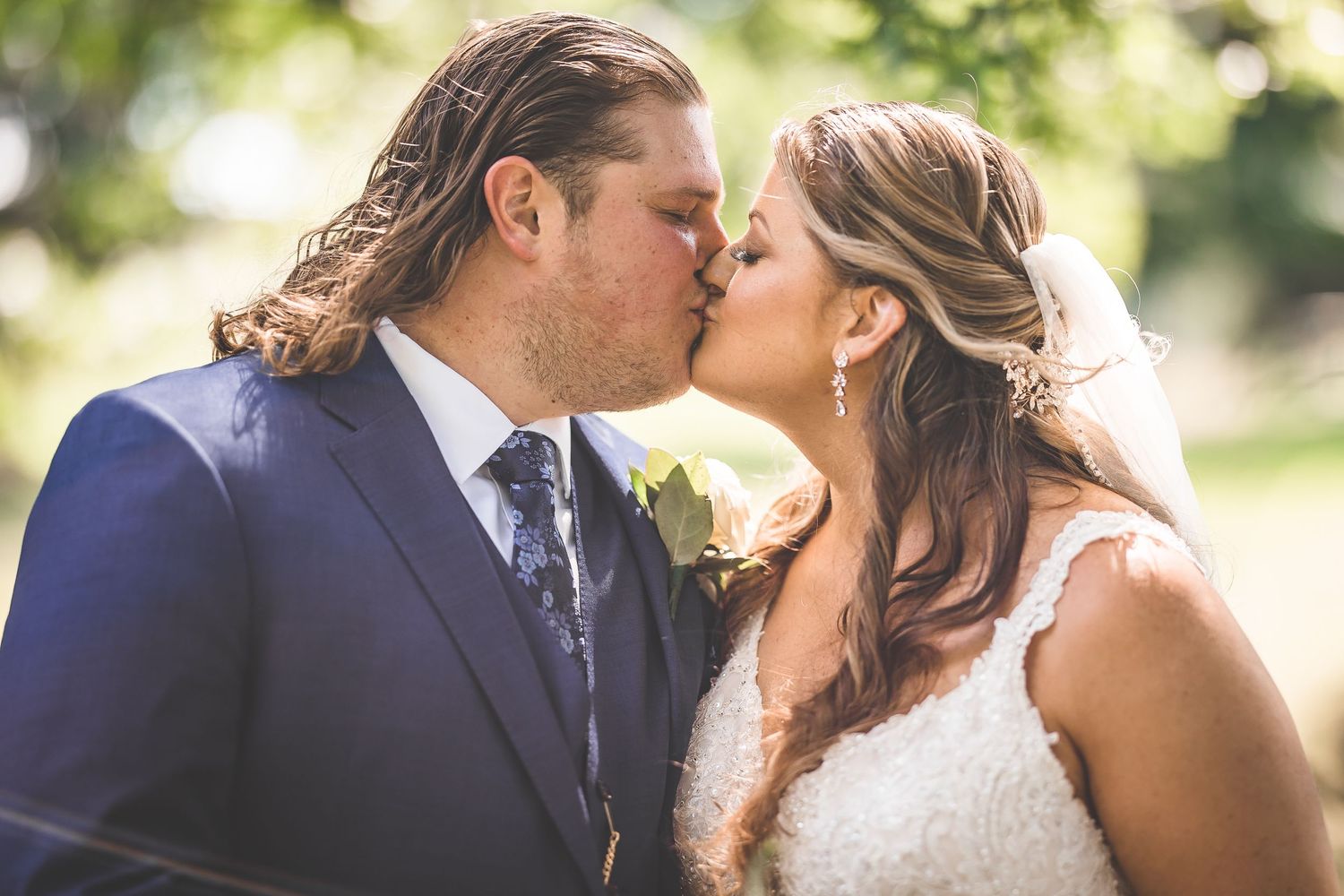 Romantic wedding couple sharing a tender kiss outdoors in natural lighting.