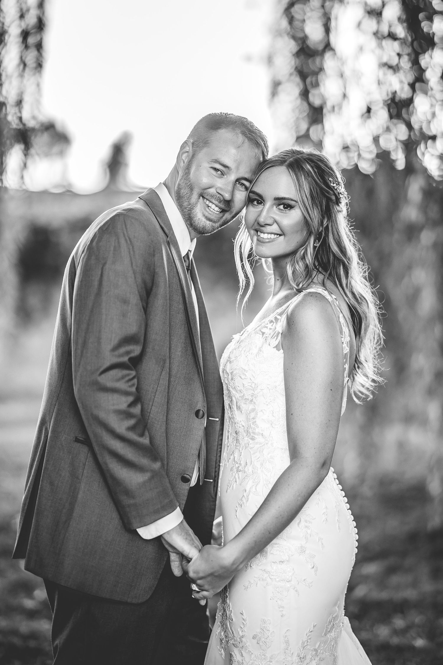 Black and white portrait of newlyweds sharing joyful laughter under willow trees.