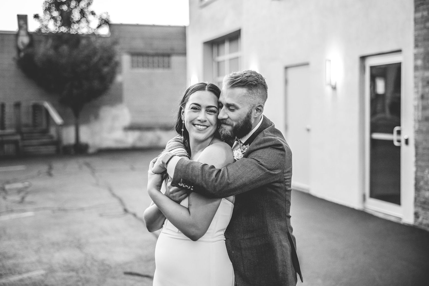 A romantic black and white portrait of a couple embracing outdoors near a white building.