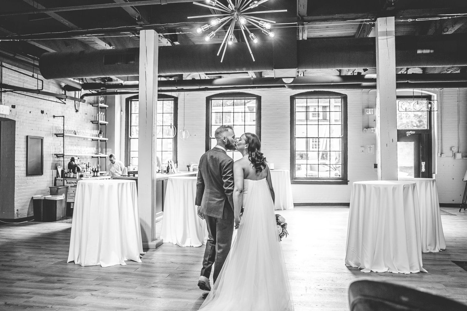 Black and white photo of industrial wedding venue with starburst chandelier.