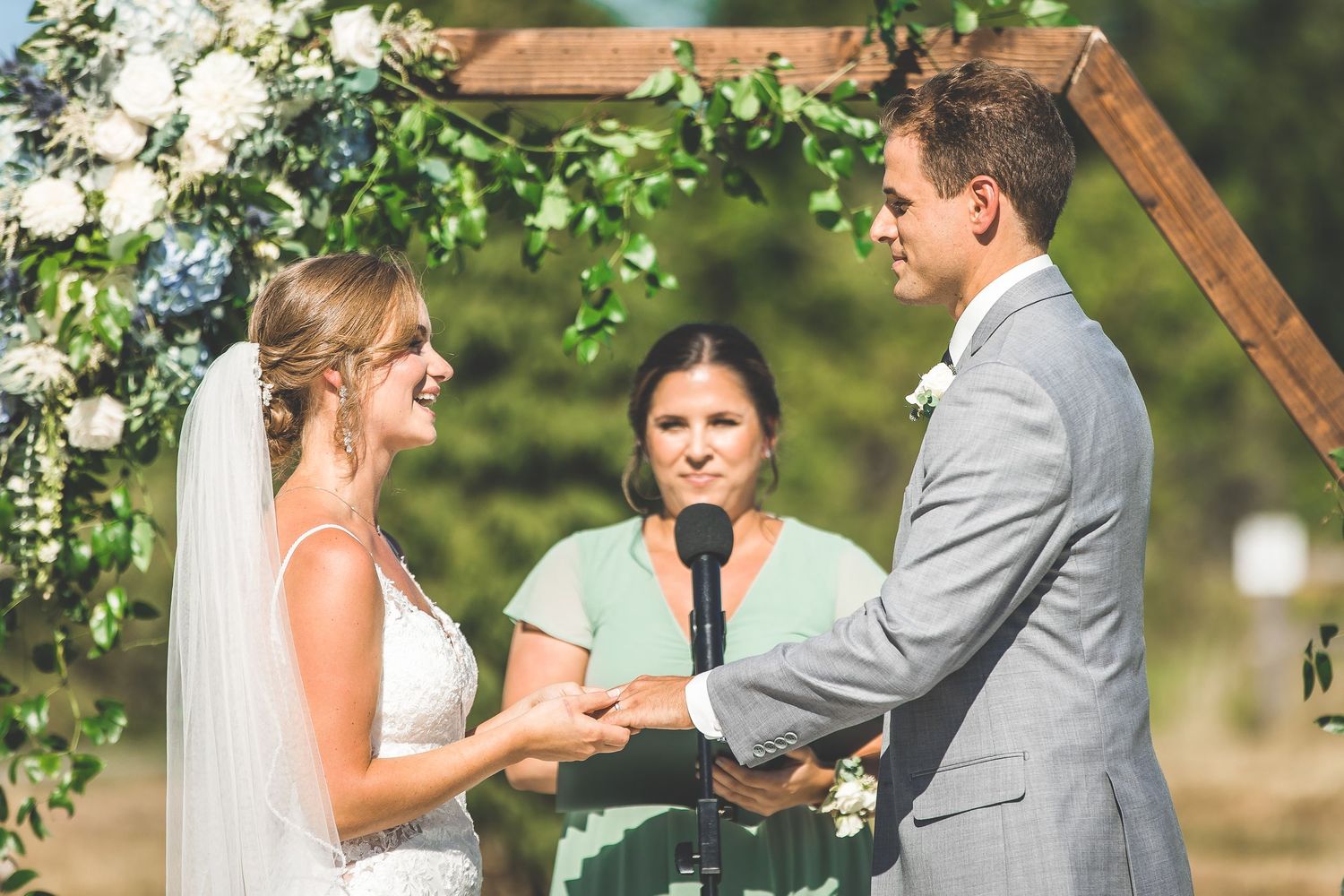 Wedding ceremony moments captured under a rustic wooden arch with white floral decorations.