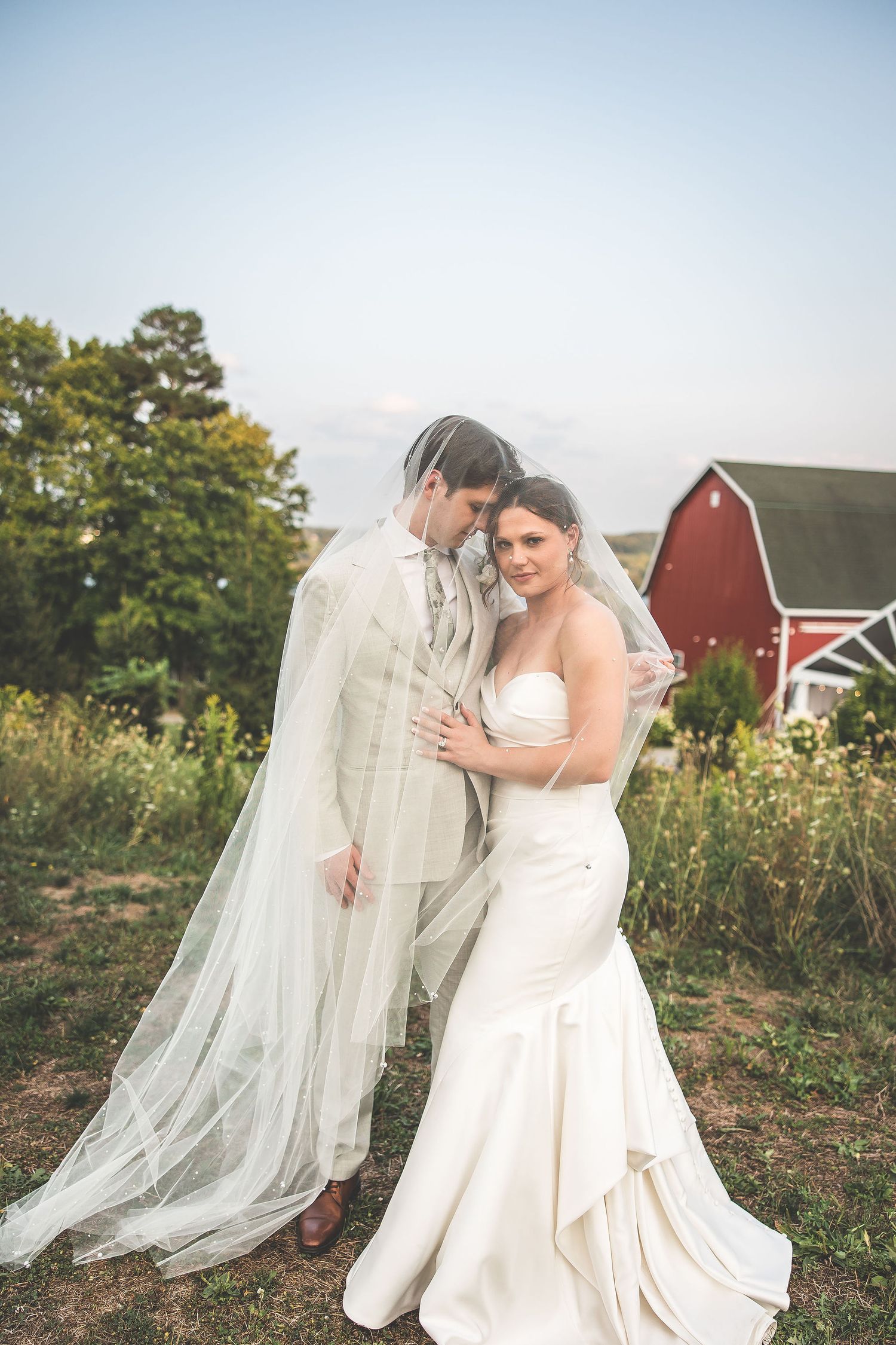 Newlyweds share an intimate moment in a rustic outdoor setting with flowing white veil.