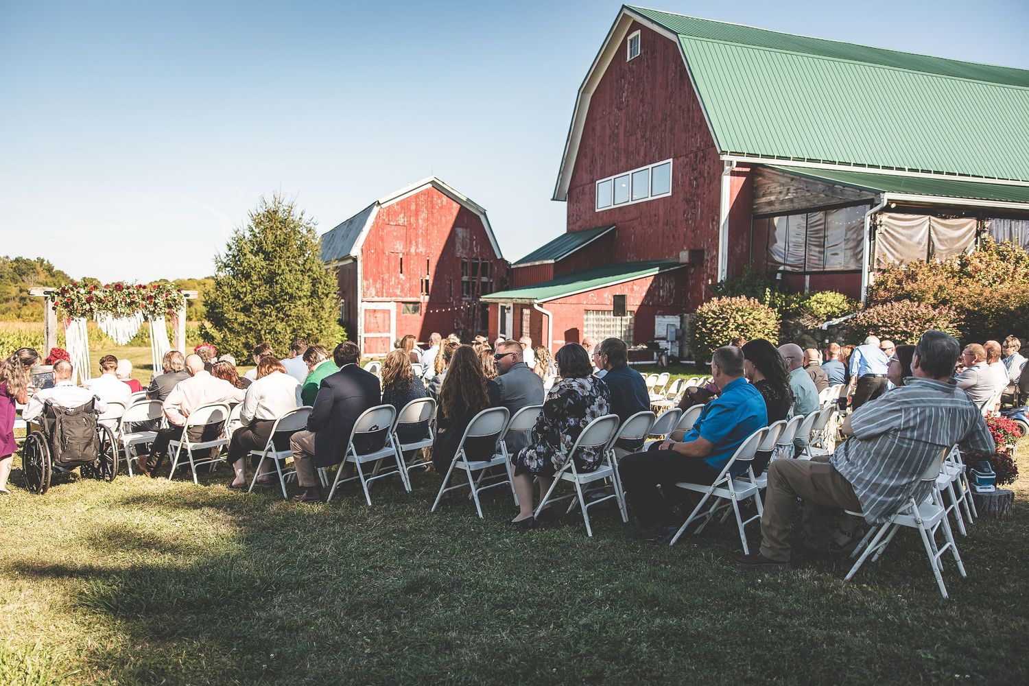 White folding chairs set up for an outdoor wedding ceremony with red barn buildings in background.
