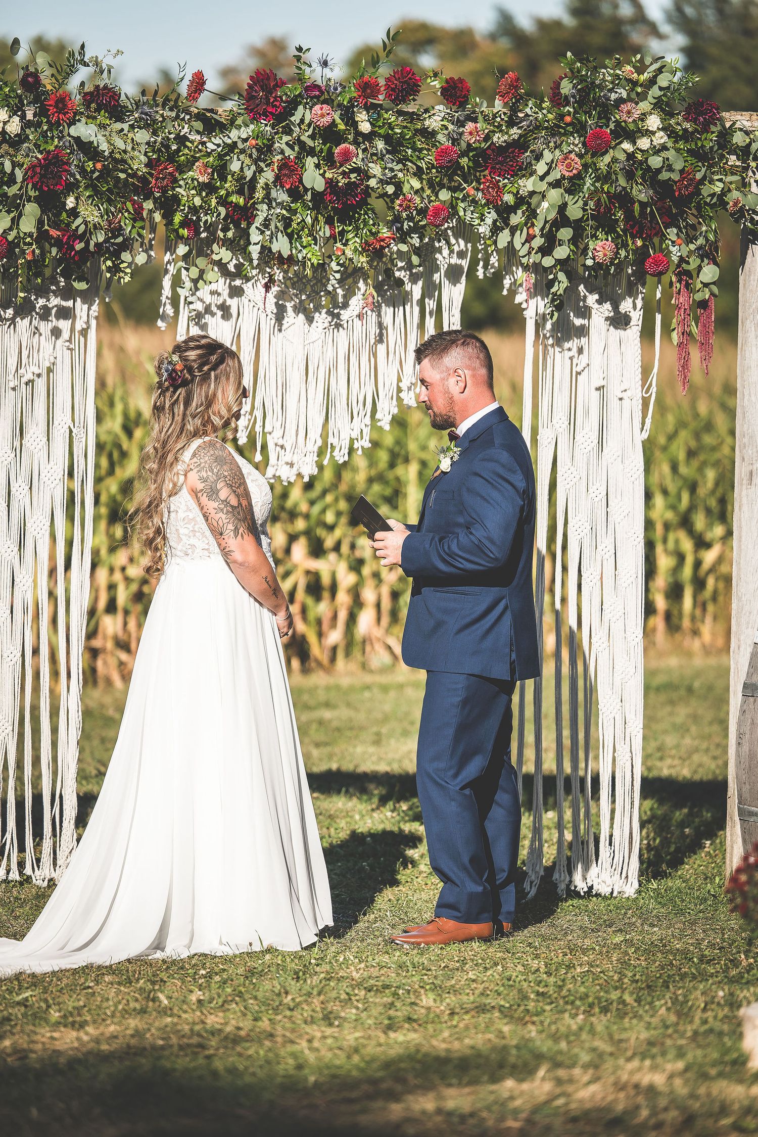 Wedding ceremony under decorative arch with flowing white fabric and red floral arrangements.