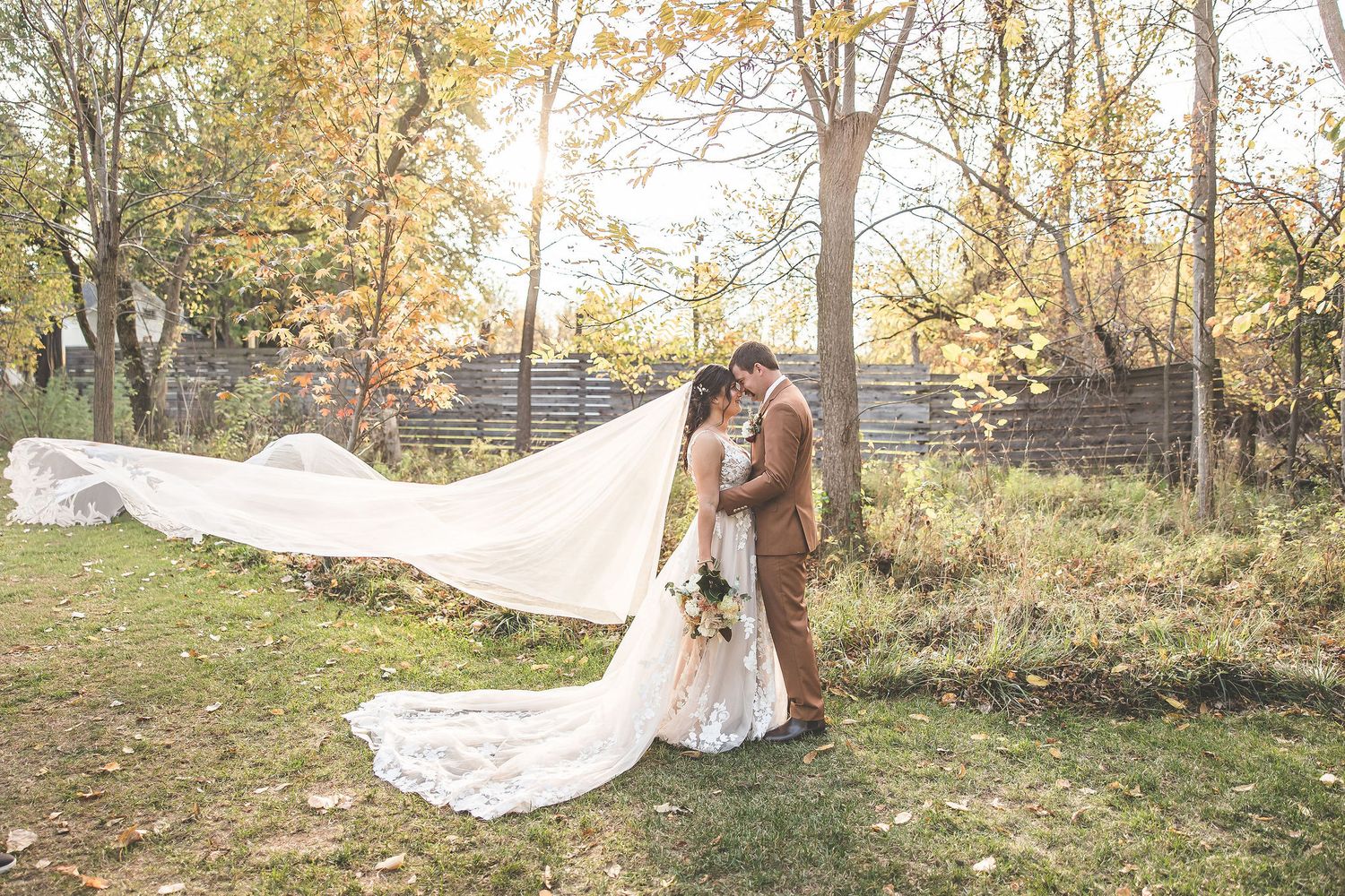 Wedding couple walks through wooded path with fallen autumn leaves.