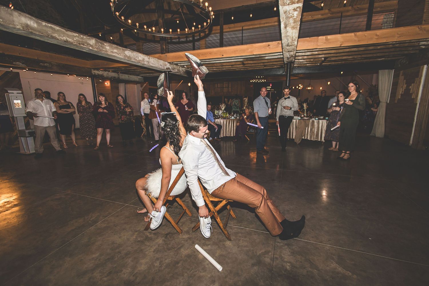 Dancers performing acrobatic moves during wedding reception on rustic wooden dance floor.