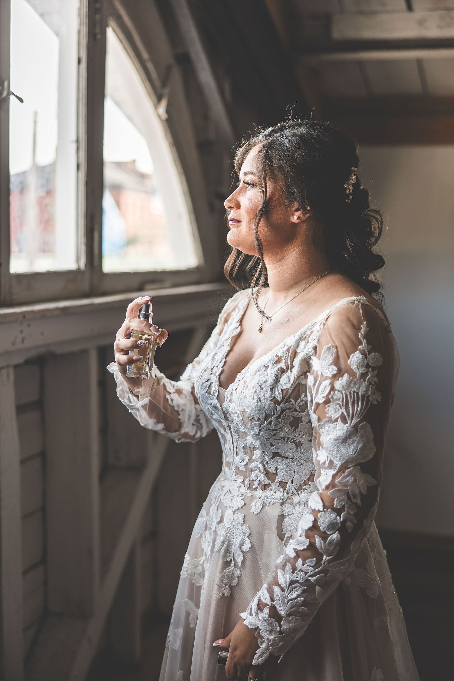 Ethereal bridal portrait by a window showing delicate lace details and flowing sleeves.