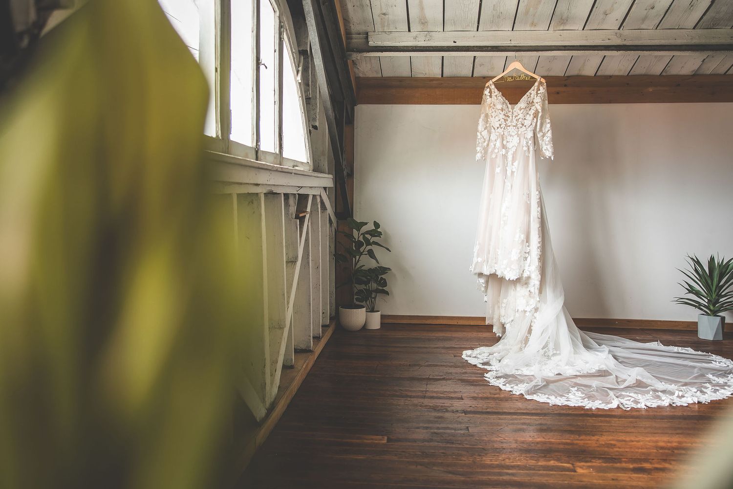 Wedding dress with intricate lace details displayed in rustic wooden room.