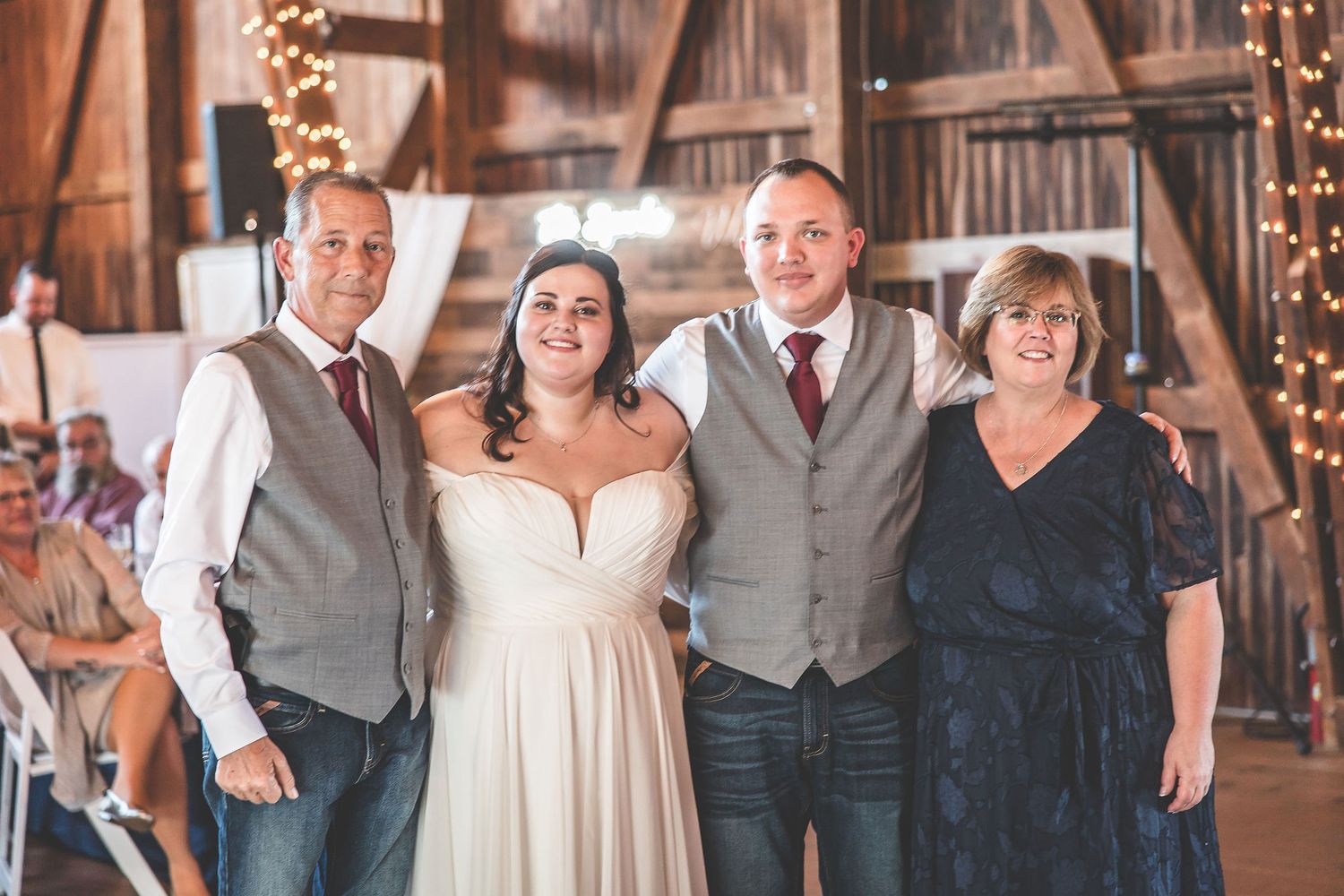 Guests celebrate at a rustic barn wedding reception with string lights and white decor.