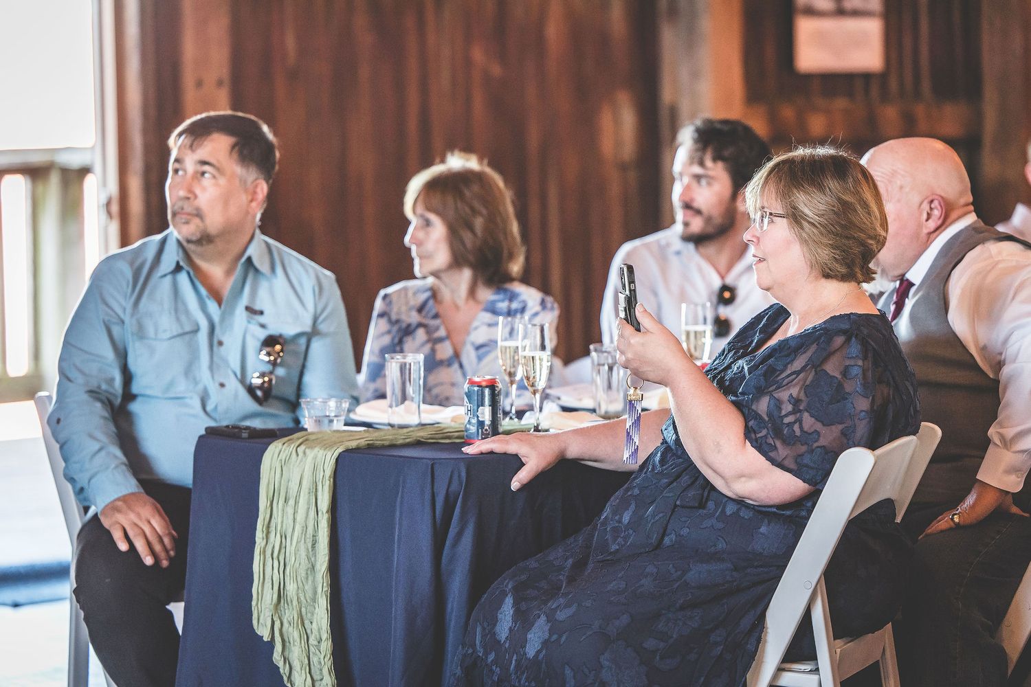 Wedding guests enjoying a reception in a rustic barn venue decorated with white curtains and string lights.