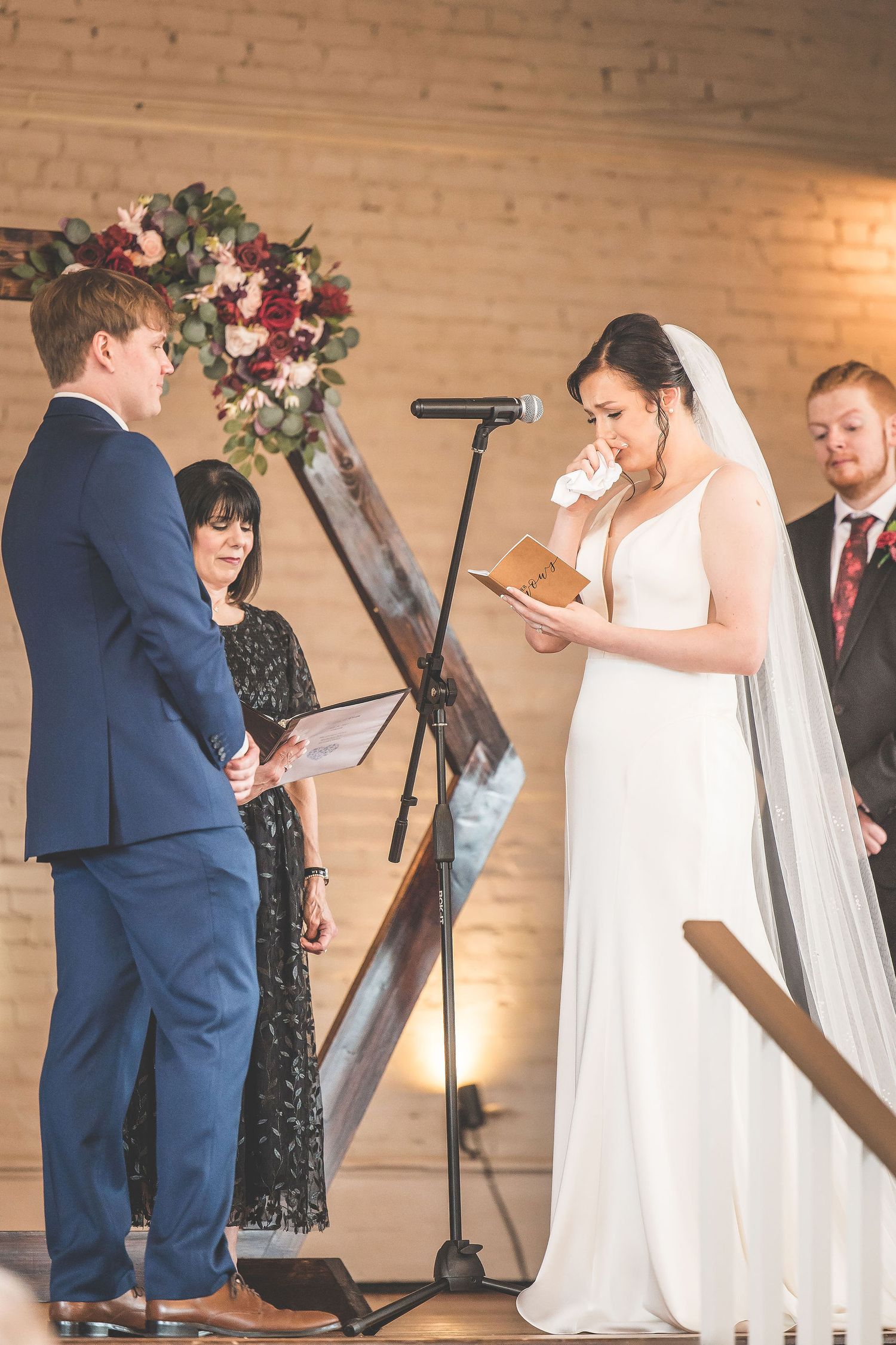 Intimate wedding ceremony moment captured against wooden geometric backdrop with flowers.