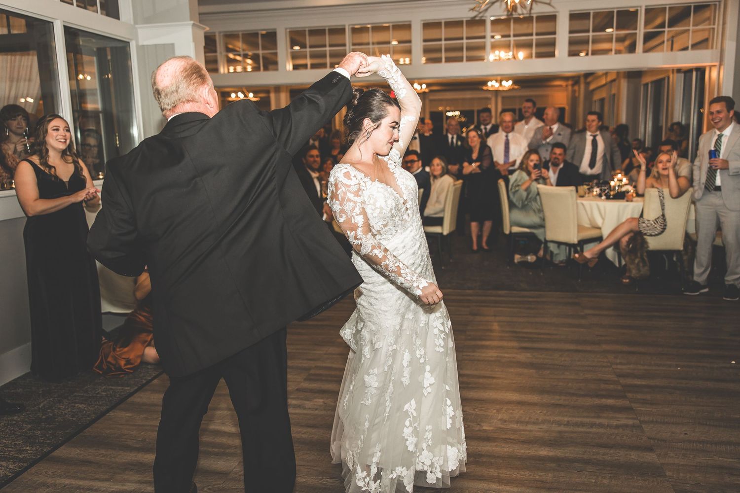 Wedding dancers twirl on a hardwood floor while guests watch from the sidelines.