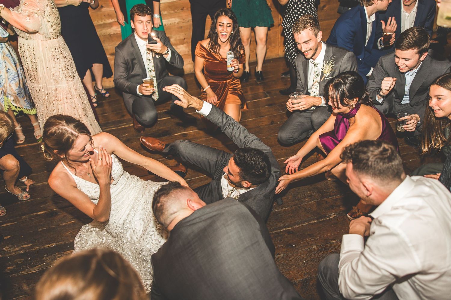 Wedding party guests dancing and celebrating on a rustic wooden floor.