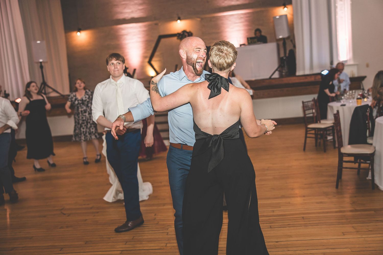 Couples dancing together during an evening wedding reception on a wooden dance floor.