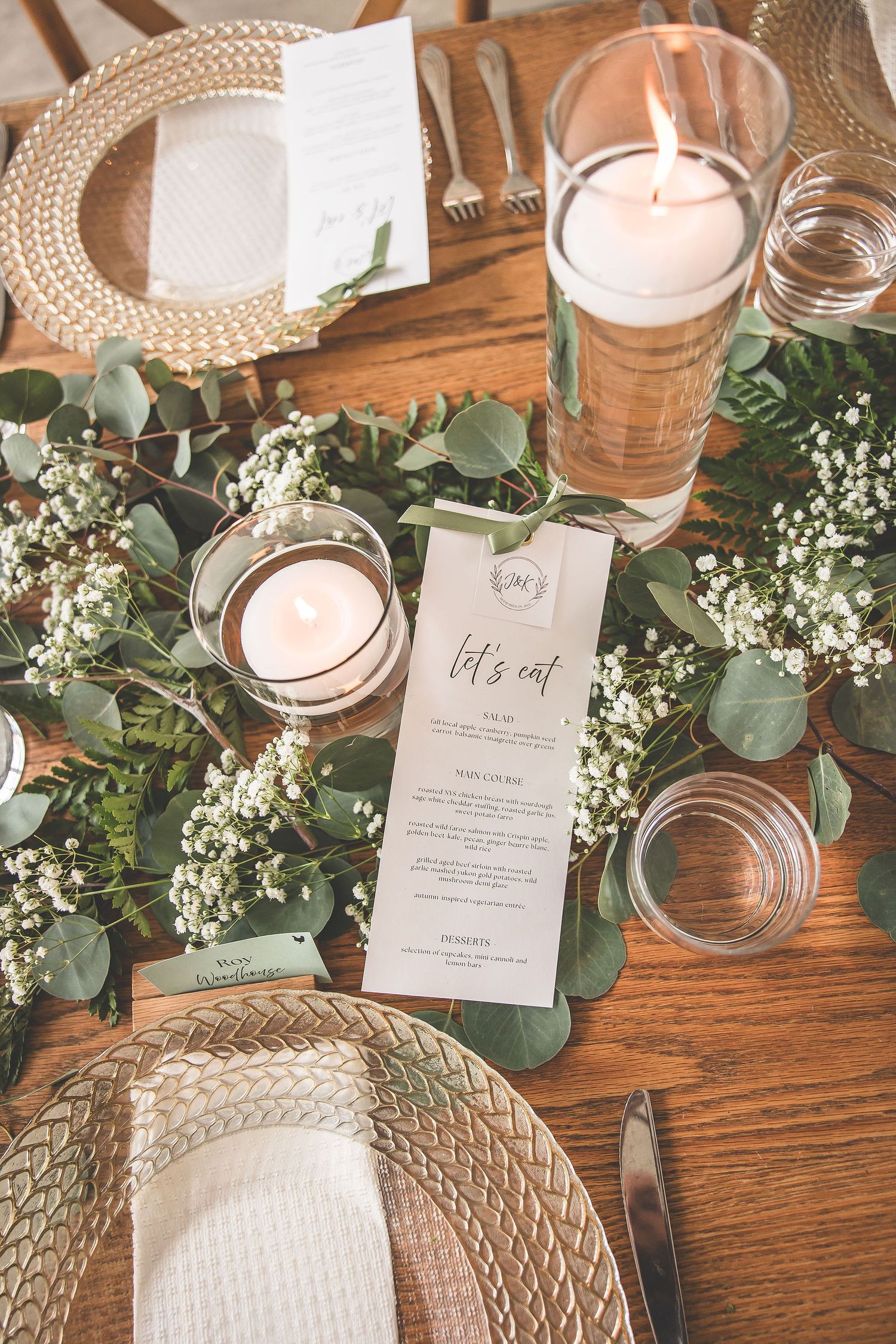 Elegant wedding table setting with woven placemats, candles, and fresh greenery on wooden surface.